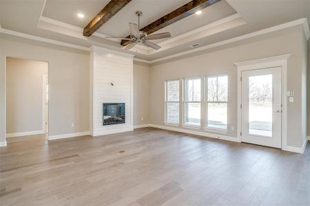 Unfurnished living room with a raised ceiling, crown molding, a fireplace, and light hardwood / wood-style flooring