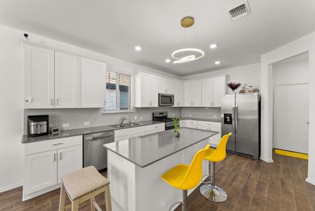 Kitchen with stainless steel appliances, a breakfast bar, visible vents, white cabinetry, and hanging light fixtures