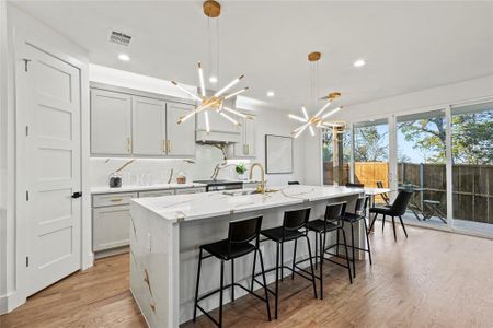 Kitchen featuring visible vents, hanging light fixtures, light stone countertops, a kitchen island with sink, and a sink