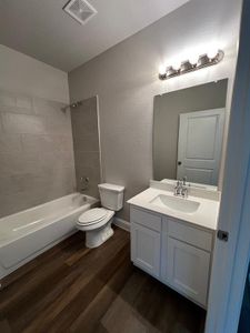 Full bathroom with hardwood / wood-style flooring, vanity, tiled shower / bath combo, and toilet