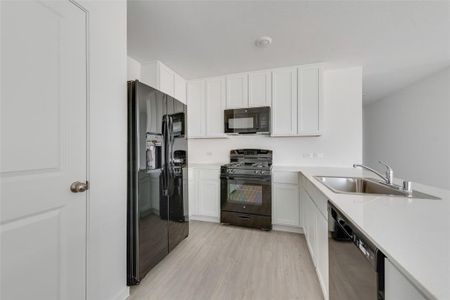 Kitchen featuring black appliances, light hardwood / wood-style floors, white cabinets, and sink