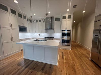 Kitchen with wall chimney exhaust hood, sink, backsplash, stainless steel appliances, and light hardwood / wood-style flooring