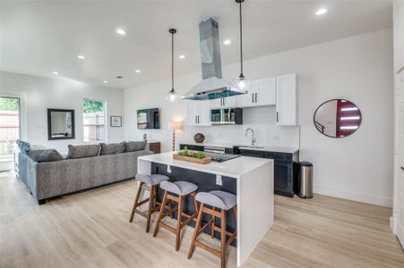 Kitchen with sink, a kitchen island, light wood-type flooring, island exhaust hood, and white cabinetry