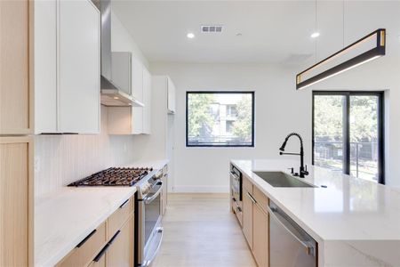 Kitchen featuring light stone counters, sink, a kitchen island with sink, wall chimney range hood, and stainless steel appliances