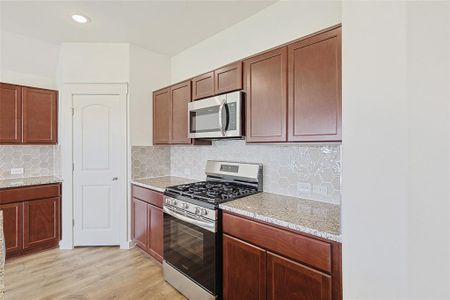 Kitchen featuring decorative backsplash, stainless steel appliances, light stone counters, and light hardwood / wood-style floors