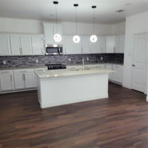 Kitchen with dark wood-type flooring, white cabinets, sink, and pendant lighting