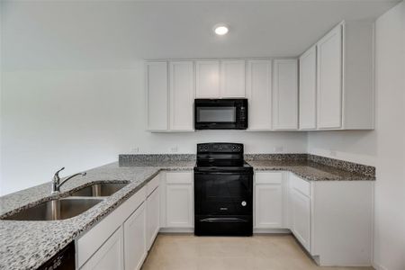 Kitchen with light stone counters, black appliances, sink, and white cabinets