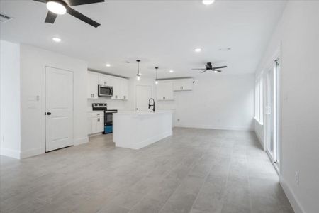 Kitchen featuring white cabinetry, an island with sink, ceiling fan, hanging light fixtures, and appliances with stainless steel finishes