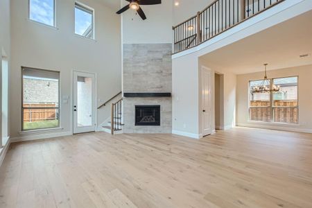 Unfurnished living room featuring ceiling fan with notable chandelier, a towering ceiling, light hardwood / wood-style floors, and a fireplace