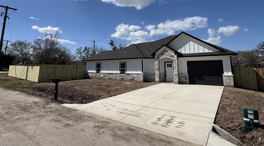 View of front of home with stone siding, fence, board and batten siding, concrete driveway, and a garage