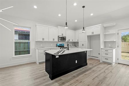 Kitchen with white cabinets, decorative light fixtures, light hardwood / wood-style floors, and a center island with sink