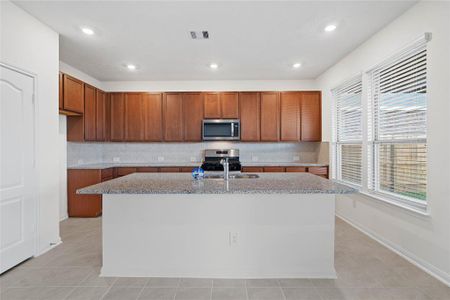 This spacious kitchen features high ceilings, stained wood cabinets, granite countertops, SS appliances, modern tile backsplash, recessed lighting, large kitchen island with space for a breakfast bar, large windows with privacyt blinds, and a pantry all overlooking your dining room and huge family room.