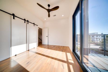 Unfurnished bedroom featuring a barn door, light wood-type flooring, and ceiling fan