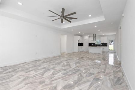 Unfurnished living room with a raised ceiling and ceiling fan