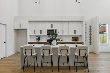 Kitchen with light hardwood / wood-style floors, white cabinets, a breakfast bar area, and an island with sink