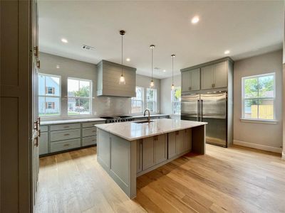 Kitchen with a healthy amount of sunlight, light stone countertops, a kitchen island with sink, and stainless steel appliances