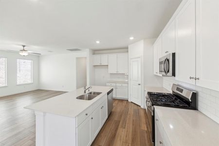 Kitchen with appliances with stainless steel finishes, a kitchen island with sink, tasteful backsplash, hardwood / wood-style flooring, and ceiling fan