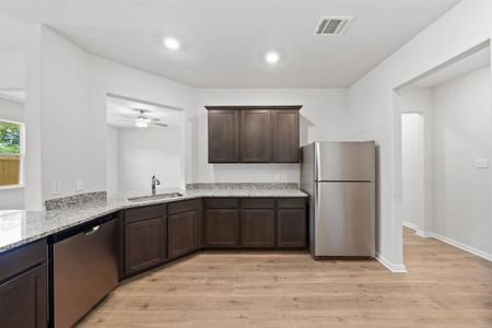 Kitchen with ceiling fan, sink, stainless steel appliances, light stone counters, and light wood-type flooring