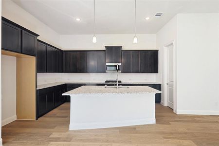 Kitchen featuring a center island with sink, light stone counters, hanging light fixtures, and light hardwood / wood-style flooring