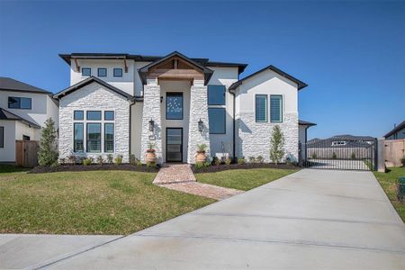 This modern two-story home features a striking facade with white stone accents and large windows. It has a welcoming entrance with a pathway, neat landscaping, and a gated driveway for added security.