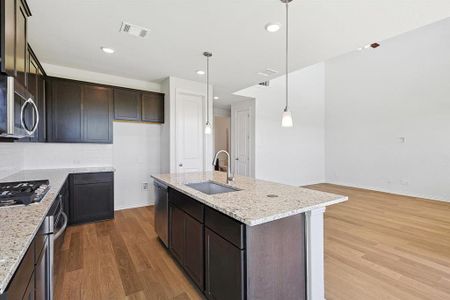 Kitchen featuring decorative light fixtures, stainless steel appliances, sink, light stone countertops, and hardwood / wood-style flooring