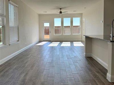 Unfurnished living room with wood tiled floor, visible vents, baseboards, and a ceiling fan