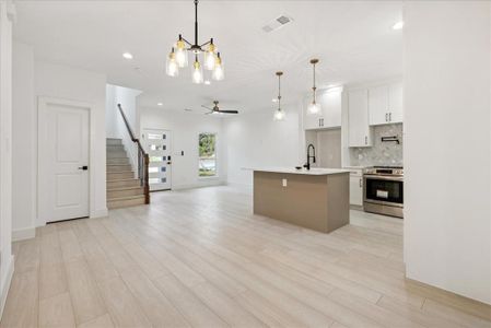 Kitchen with white cabinets, stainless steel range with electric cooktop, a center island with sink, light hardwood / wood-style flooring, and decorative light fixtures