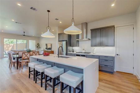 Kitchen featuring sink, decorative light fixtures, decorative backsplash, light wood-type flooring, and wall chimney exhaust hood