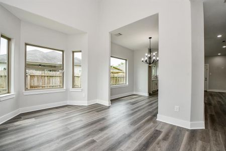 This is a spacious view of living and dinning rooms featuring elegant gray wood flooring, fresh white walls, ample natural light from large windows, and a stylish chandelier that adds a touch of sophistication. The open floor plan allows for versatile furnishing options.