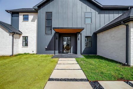 View of exterior entry featuring board and batten siding, brick siding, a lawn, and roof with shingles