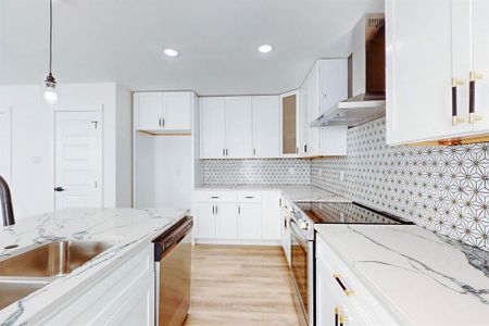 Kitchen with appliances with stainless steel finishes, hanging light fixtures, wall chimney range hood, and white cabinets