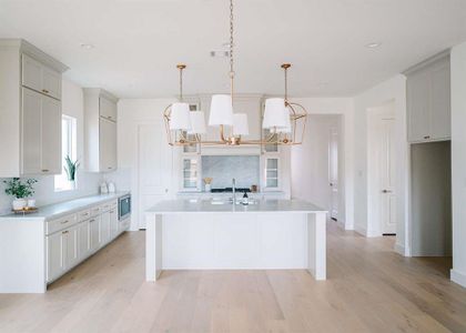 Kitchen featuring stainless steel microwave, backsplash, a center island with sink, hanging light fixtures, and a notable chandelier