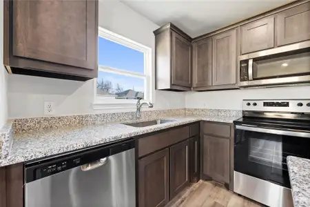 Kitchen with appliances with stainless steel finishes, a sink, dark brown cabinetry, light wood-style floors, and light stone countertops Kitchen with appliances with stainless steel finishes, a sink, dark brown cabinetry, light wood-style floors, and light stone countertops
