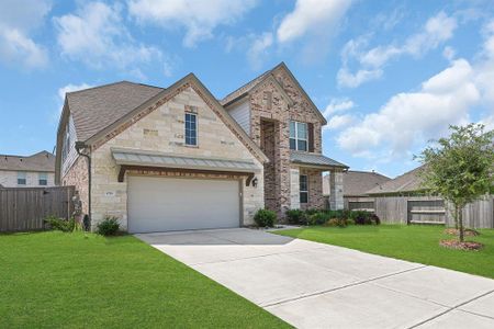 This is a modern two-story home with a mix of stone and brick facade, featuring a two-car garage and a well-manicured lawn.