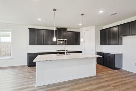 Kitchen with a center island with sink, light hardwood / wood-style flooring, light stone counters, and decorative light fixtures