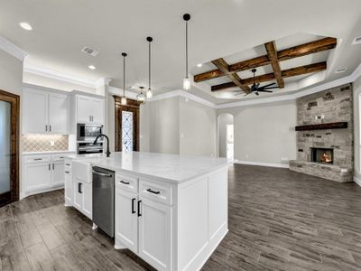 Kitchen with white cabinets, coffered ceiling, a kitchen island with sink, light stone counters, and stainless steel appliances