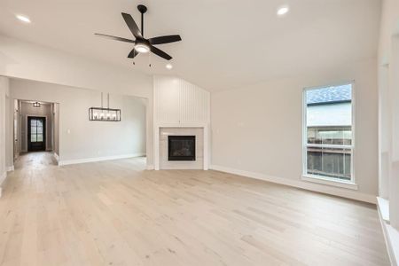 Unfurnished living room featuring light wood-type flooring, a large fireplace, and ceiling fan with notable chandelier