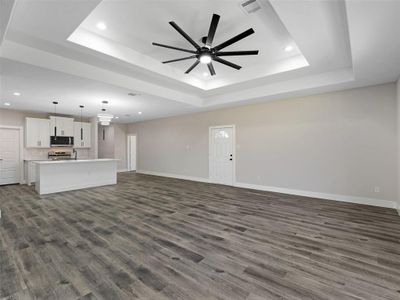 Unfurnished living room with dark hardwood / wood-style flooring, a raised ceiling, and ceiling fan