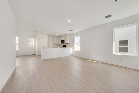 Unfurnished living room featuring light wood-type flooring, plenty of natural light, visible vents, and baseboards