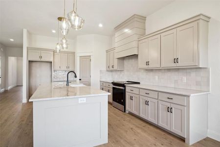 Kitchen with light wood-type flooring, tasteful backsplash, a kitchen island with sink, sink, and stainless steel range oven