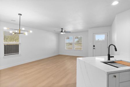 Kitchen featuring hanging light fixtures, light stone counters, sink, light hardwood / wood-style flooring, and ceiling fan with notable chandelier