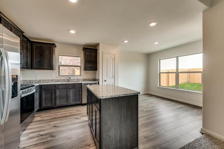 Kitchen with a kitchen island, light stone countertops, dark brown cabinets, light wood-type flooring, and appliances with stainless steel finishes