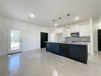 Kitchen with white cabinets, sink, tasteful backsplash, a kitchen island with sink, and light stone countertops