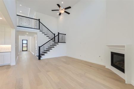 Unfurnished living room featuring light wood-type flooring, a high ceiling, and ceiling fan