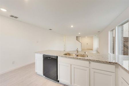 Kitchen with white cabinetry, sink, light stone counters, and black dishwasher