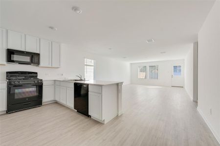 Kitchen with white cabinets, kitchen peninsula, black appliances, and light hardwood / wood-style flooring