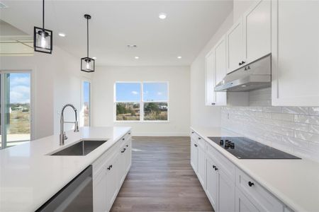 Kitchen with sink, stainless steel dishwasher, decorative light fixtures, black electric cooktop, and white cabinets