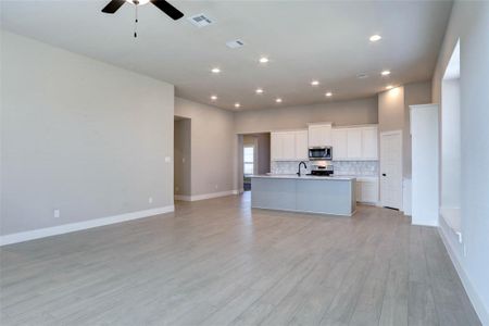 Kitchen featuring an island with sink, sink, white cabinets, backsplash, and ceiling fan