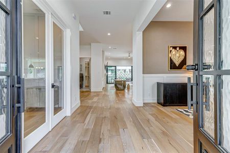 This inviting home features a bright and spacious entryway with hardwood floors, modern decor, and an open layout leading to a living area. Glass doors and ample natural light enhance the welcoming atmosphere.