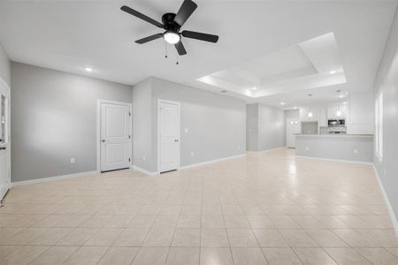 Unfurnished living room with a tray ceiling, ceiling fan, and light tile patterned flooring